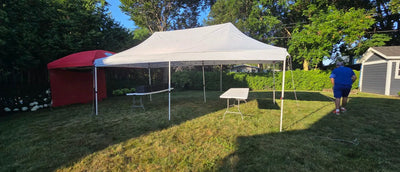 A white pop-up canopy tent is set up on a grassy backyard lawn, with a red shed for rentals.