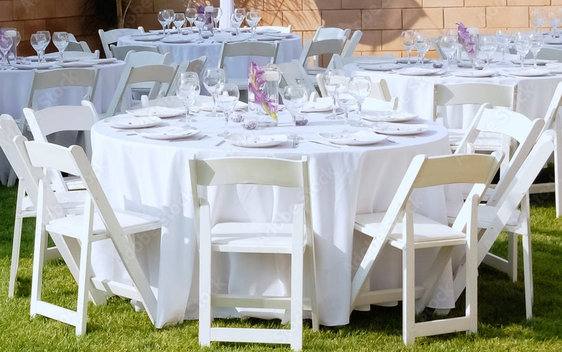 Outdoor event setup with round tables, white folding chairs, linens, glassware, and tableware rentals from One Party Rentals for weddings and celebrations.